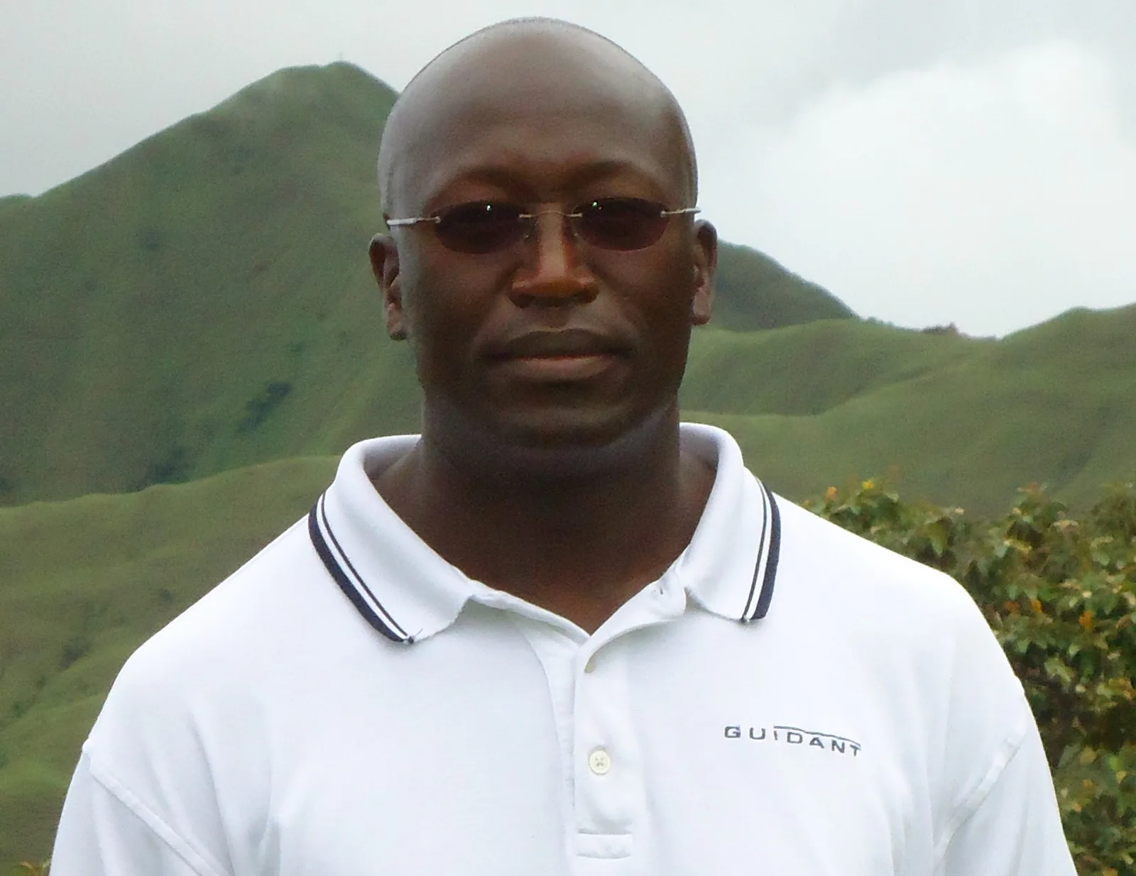 Abel Ndambasha standing outdoors with green hills behind him