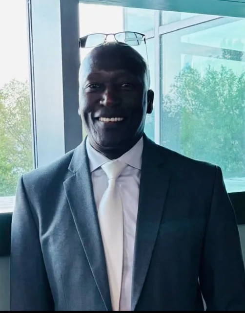 Abel Ndambasha smiling in a dark suit and light tie