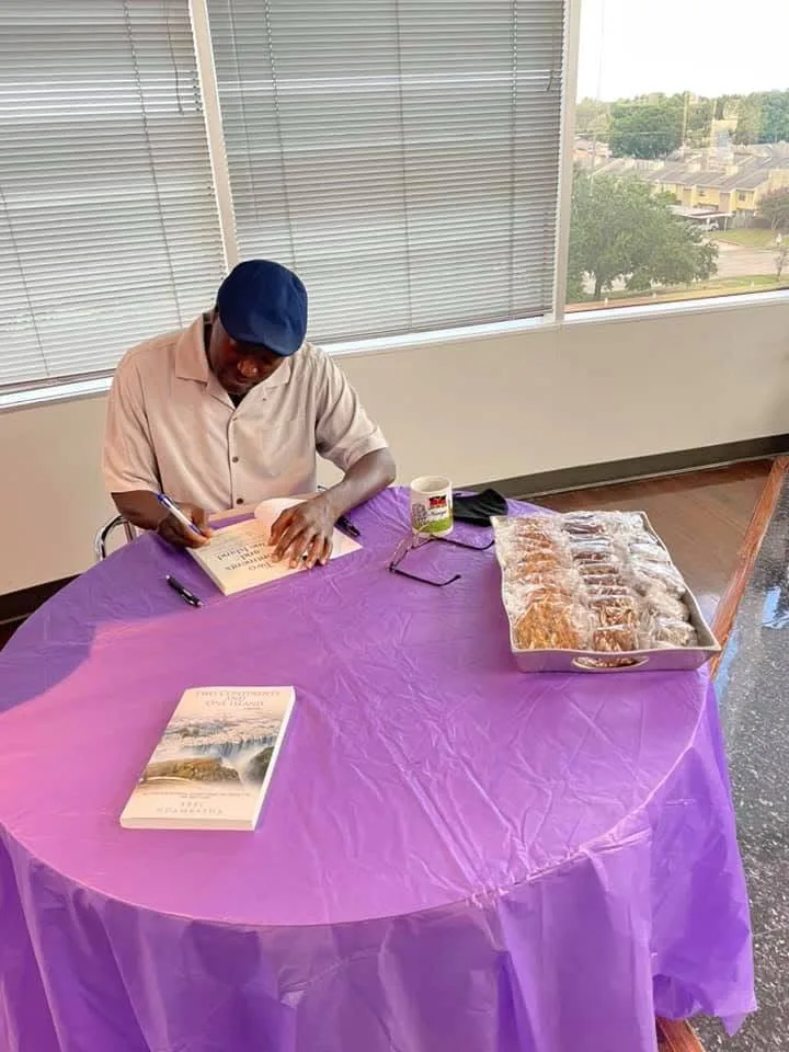 Abel Ndambasha signing a copy of his memoir at a table